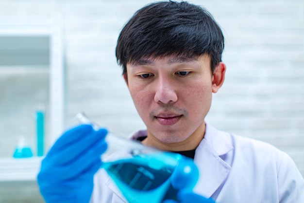 Closeup shot of syringe needle sucking coronavirus covid19 vaccine from glass vial bottle for injection by asian professional male scientist in white lab coat wearing face mask in blurred background