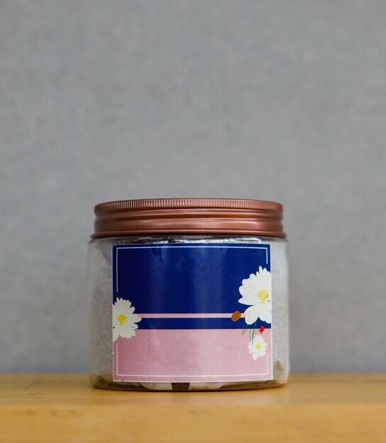 Closeup shot of traditional Chinese dry spices and herbs ingredient in glass jar with cap no brand for commercial advertisement text on blue and pink with blossom flower label placed on wooden table.