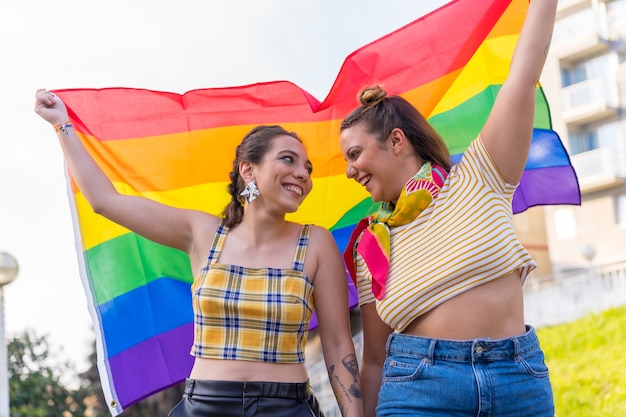 屋外で高いLGBTプライドフラグを保持している2人の若い白人女性のクローズアップショット