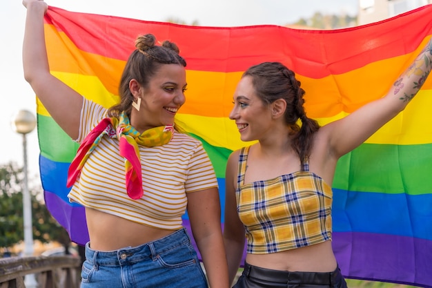 A closeup shot of two young Caucasian females holding high LGBT pride flag outdoors