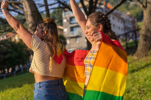 야외에서 LGBT 프라이드 깃발을 들고 있는 두 젊은 백인 여성의 근접 촬영