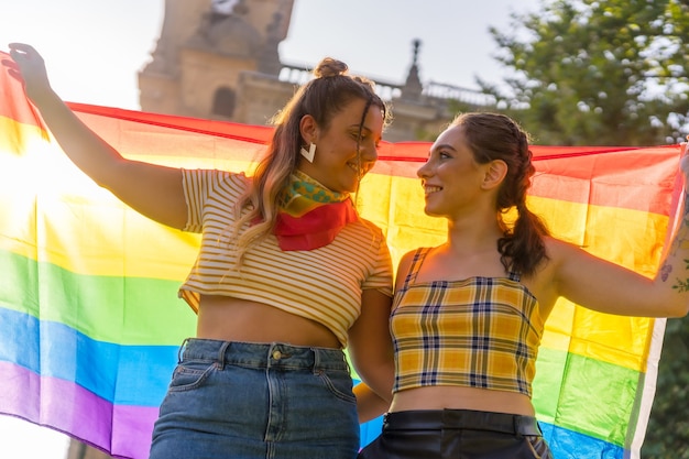 LGBTプライドフラグを屋外で保持している2人の若い白人女性のクローズアップショット