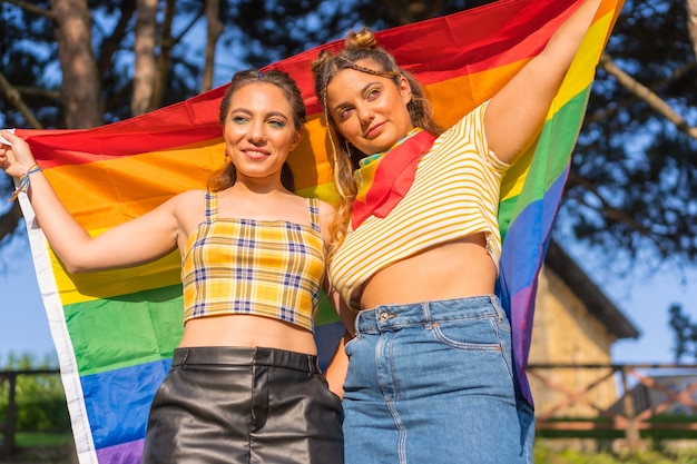 A closeup shot of two young Caucasian females holding LGBT pride flag outdoors