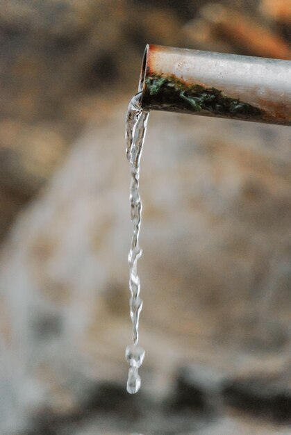 Крупный план воды, вытекающей из металлической трубы в скалах