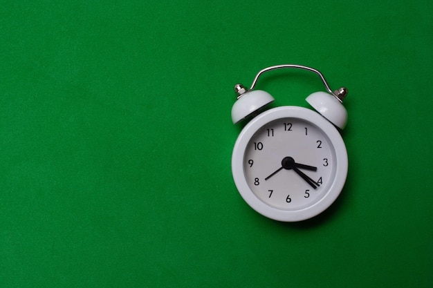 Closeup shot of a white clock on a green surface with a copy space