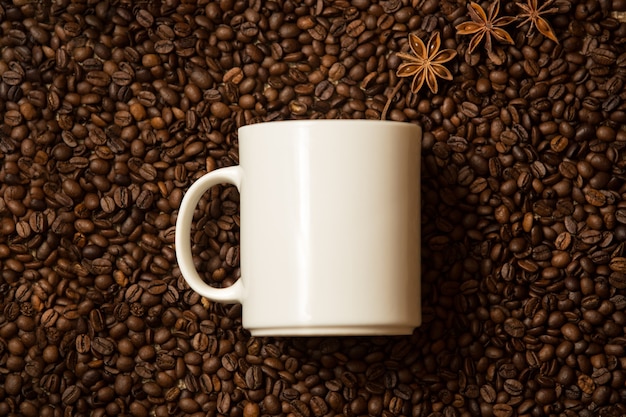 Closeup shot of white mug against coffee beans with anise stars lying like steam