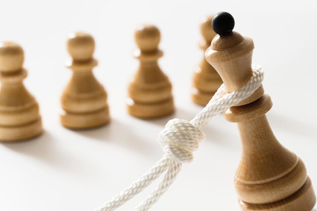 Closeup shot of a white rope pulling down a wooden chess queen with several chessmen nearby Concept of facing public disapproval and being burdened by responsibility