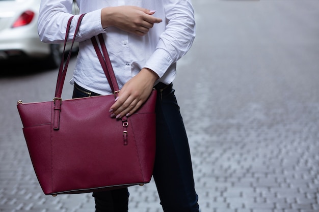 Closeup shot of woman holding big red leather purse. Empty space