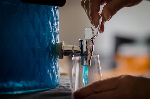Closeup shot of a woman\'s hand pouring blue juice from a\
tap