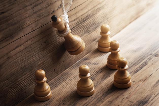 Closeup shot of a wooden chess queen hanging on a white rope with pawns standing below Concept of facing public disapproval and being burdened by responsibility