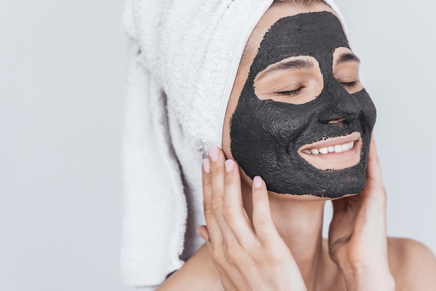 Closeup shot of young beautiful female applying black clay mask doing beauty wellness treatment on her face skin Horizontal shot of female applying organic facial mask with closed eyes on white