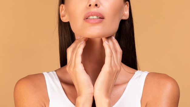 Closeup shot of young woman suffering from pain in throat touching her neck panorama beige studio background