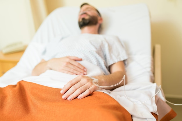 Closeup of sick male patient with IV drip on hand lying over bed in hospital