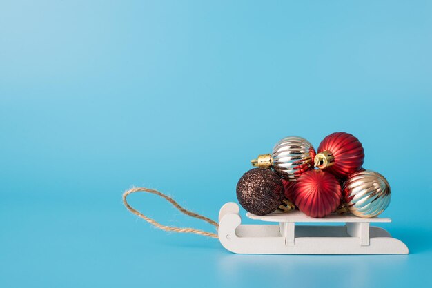 Closeup side profile view photo of toy small sledges carrying heap pile stack of Christmas balls isolated over light background with empty blank space