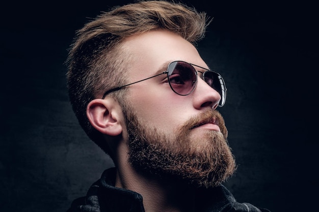 Closeup side view of bearded male in sunglasses on grey vignette background.