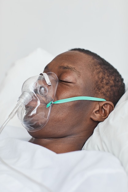 Closeup side view portrait of African-American man in hospital bed with oxygen mask