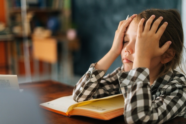 Closeup side view of sad exhausted primary child school girl tired from studying holding head head