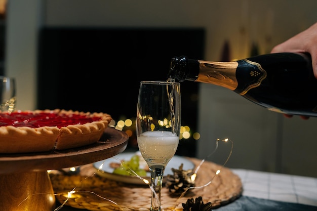 Photo closeup side view of unrecognizable man pouring champagne into glass at dinner feast table during family party on blurred background bokeh lights concept of preparation to holiday celebration