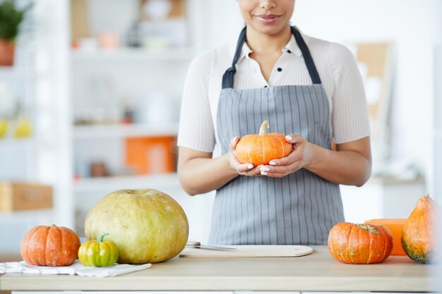 Primo piano di una donna esperta in grembiule in piedi al bancone e scegliendo la zucca per fare jackolantern