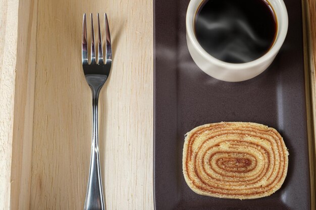 Closeup of a slice of bolo de rolo on a brown plate, next to cup of coffee and a fork.