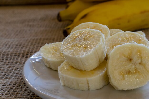 접시에 얇게 썬 바나나를 닫고 배경에 바나나 한 뭉치를 닫습니다. 선택적 초점