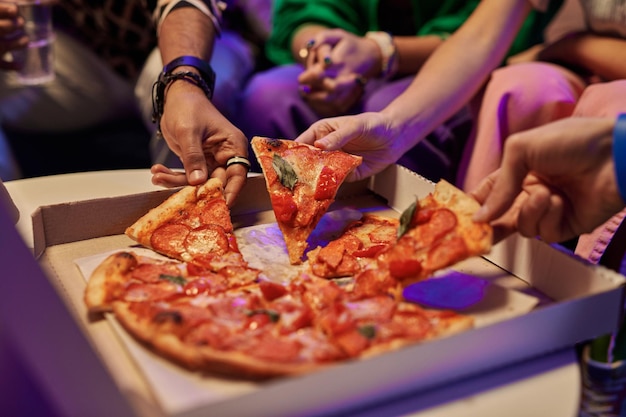 Photo closeup of slices of appetizing pizza in box being eaten by friends