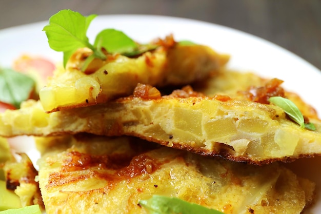 Primo piano fette di frittata spagnola o tortilla de patatas guarnite con foglie di basilico fresco