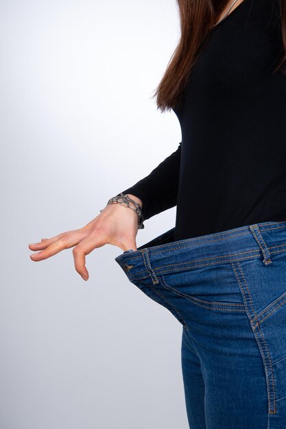 흰색 배경 다이어트 개념 복사 공간에 고립 된 성공적인 체중 감량을 보여주는 큰 청바지에 젊은 여성 모델의 슬림 허리의 근접 촬영