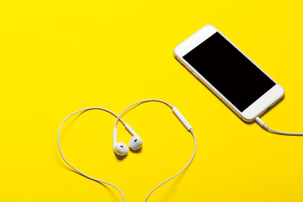 Closeup of smart phone with headphones on a yellow background Top view Listen to music