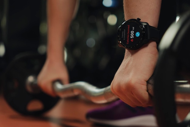 Closeup of a smart watch on womans hand lifting a heavy barbell in the gym on a dark background burn
