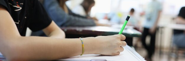 Photo closeup of smiling girl sitting at school desk and writing pupil drawing in album education art