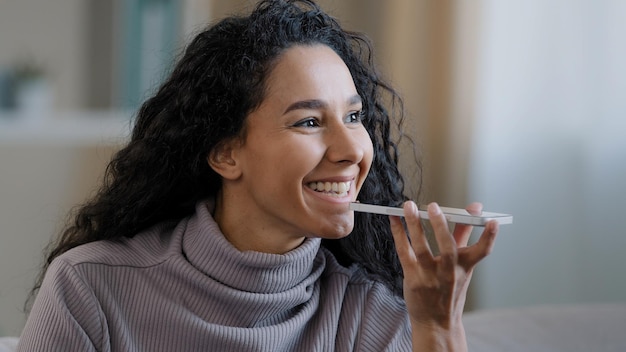 Closeup smiling happy young woman talk on speakerphone record audio message using telephone hispanic