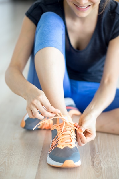 Closeup of Smiling Woman Tying Shoelace on Floor