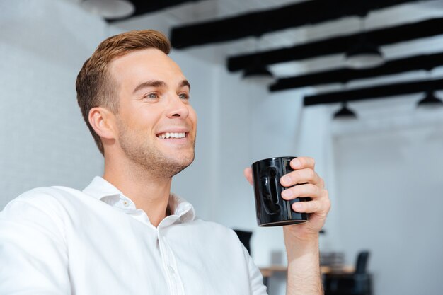 座って、オフィスでコーヒーを飲む笑顔の若いビジネスマンのクローズアップ