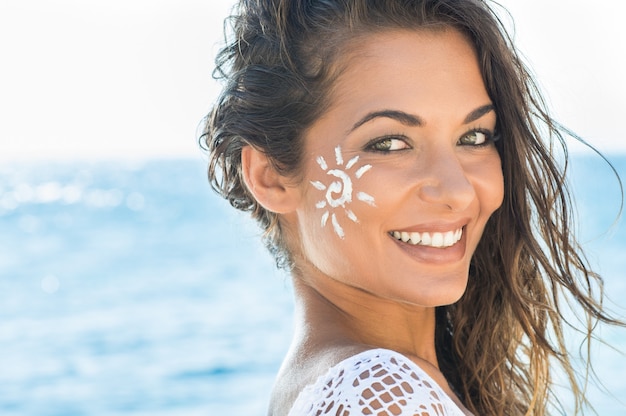 Primo piano di giovane donna sorridente con crema solare sul viso in mare