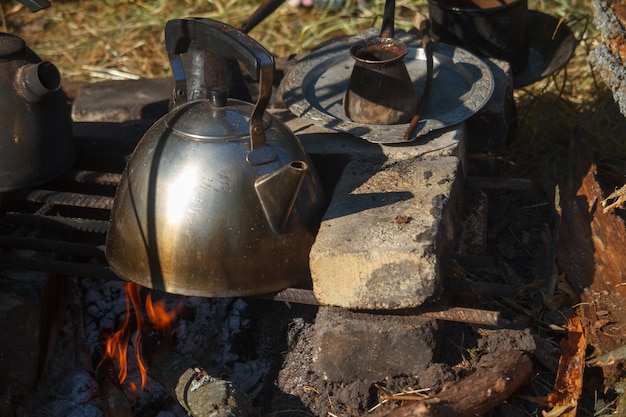 Bollitore del metallo affumicato primo piano su un forno casalingo sopra il fuoco e il cezva con caffè appena preparato