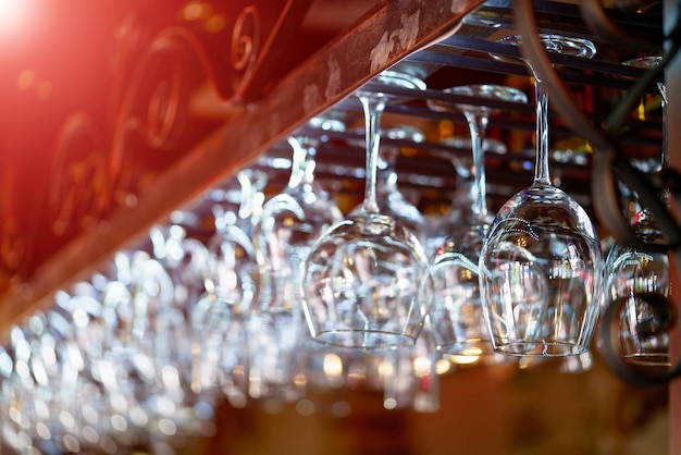 Closeup of some clean wine glasses hung on the bar at a restaurant over the blurred background with red light leaks Glasses prepared for a party at the bar