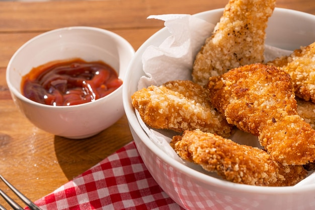 Closeup of some fried chicken nuggets in a white bowl accompanied by kétchup sauce