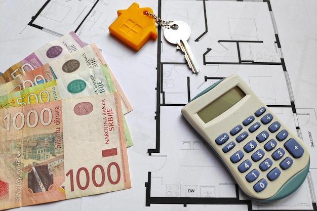 일부 세르비아 디나르 지폐에 집 열쇠와 건축 계획 맨 위에 있는 계산기를 닫습니다.