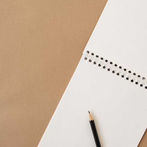 Closeup of spiral notebook and pencil on neutral beige pastel. Blank paper sheet copy space template. Flat lay, top view.