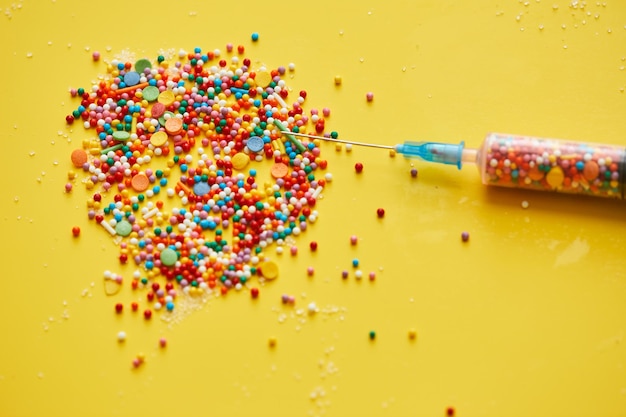 Closeup of splattering sweet sprinkles and needle of medical syringe on bright yellow background