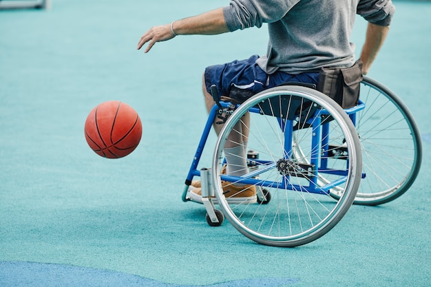 Primo piano dello sportivo con disabilità seduto in sedia a rotelle che gioca a basket all'aperto