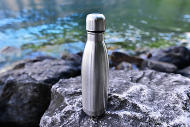 Photo closeup of steel eco thermo water bottle on the surface of the lake in the mountains