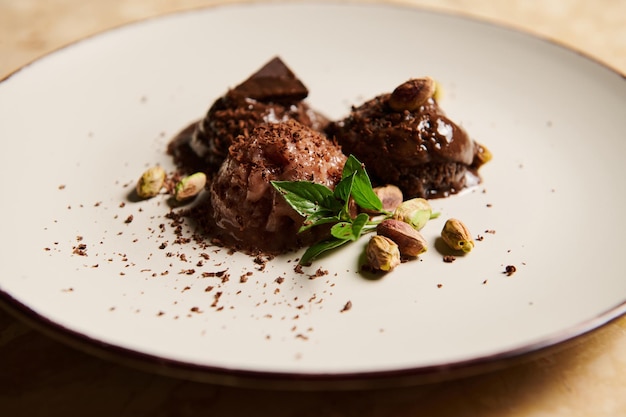 Closeup Still life Frozen balls of chocolate ice cream with pistachio and lemon basil leaves melting on white plate