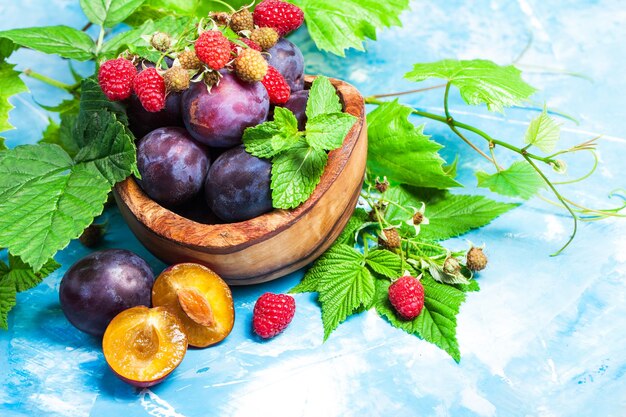 Photo closeup still life of plums and red raspberry with green leaves