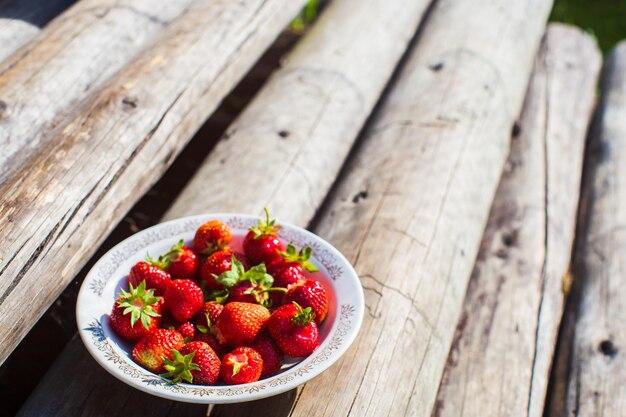 Closeup strawberry crop lying in a plate on rural wooden steps The concept of healthy food vitamins agriculture market strawberry sale