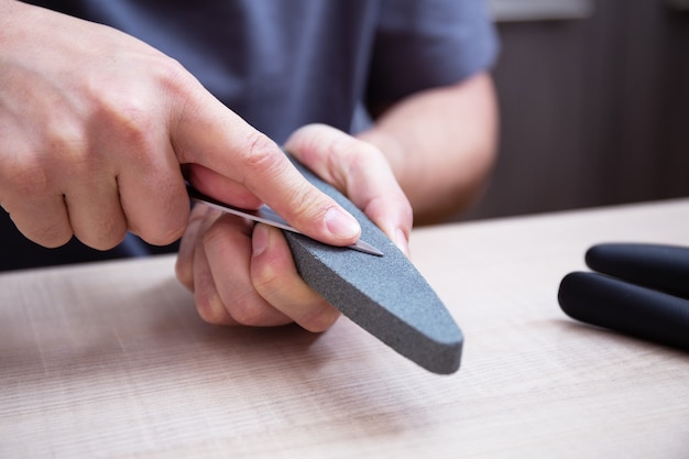 Closeup strong male hands sharpen a kitchen metal knife with a grindstone Home household knife sharpening