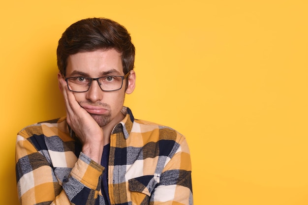 Closeup studio portrait of upset tired guy in glasses looking at camera isolated on yellow background. Boring, dull, tedious concept. Human emotions, facial expression. Overworked unhappy man