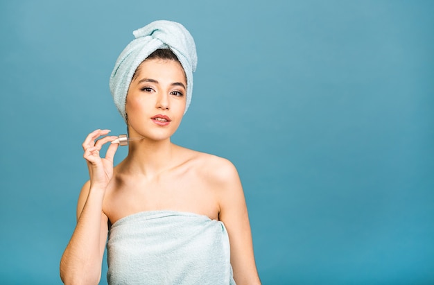 Closeup studio portret met jonge vrouw in badhanddoek op hoofd geïsoleerd op kopie ruimte olie serum uit pipet toe te passen.