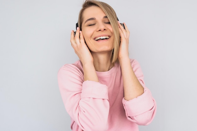 Closeup studio portret van gelukkige jonge vrouw draagt roze kleren met gesloten ogen met koptelefoon met handen luisteren favoriete muziek geïsoleerd op witte achtergrond kopie ruimte voor advertentie